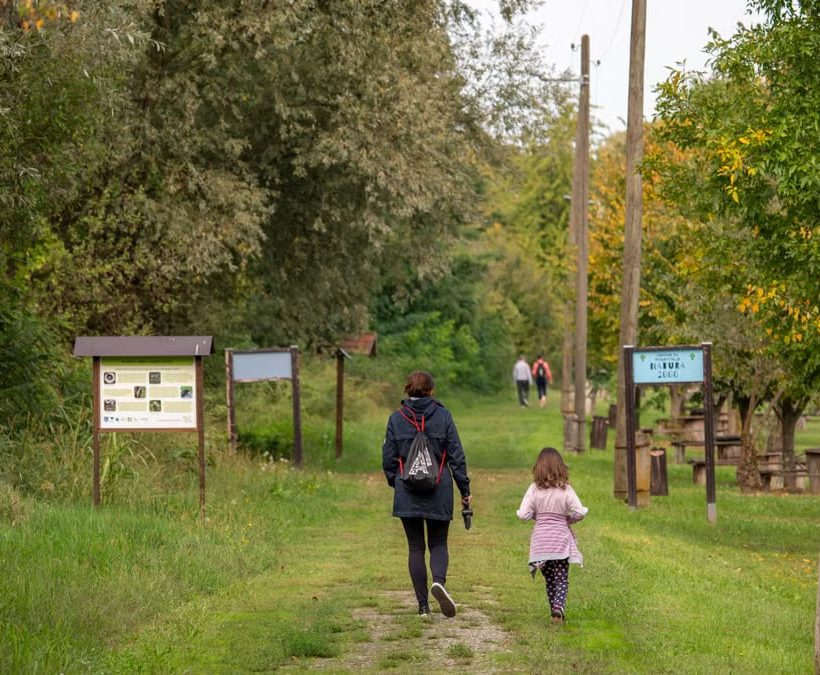 A parent and child walking on a path in a scenic nature reserve in Croatia, surrounded by lush greenery.