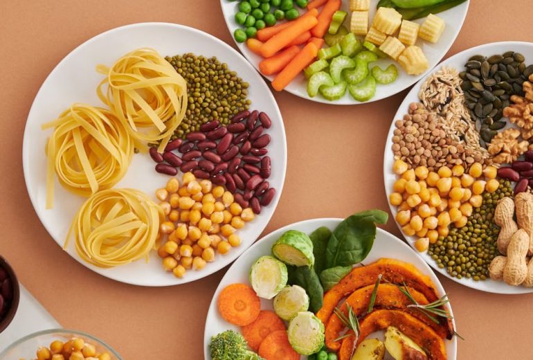 A vibrant mix of legumes, vegetables, nuts, and pasta arranged on white plates showcasing a balanced, healthy diet.