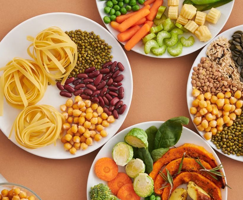 A vibrant mix of legumes, vegetables, nuts, and pasta arranged on white plates showcasing a balanced, healthy diet.
